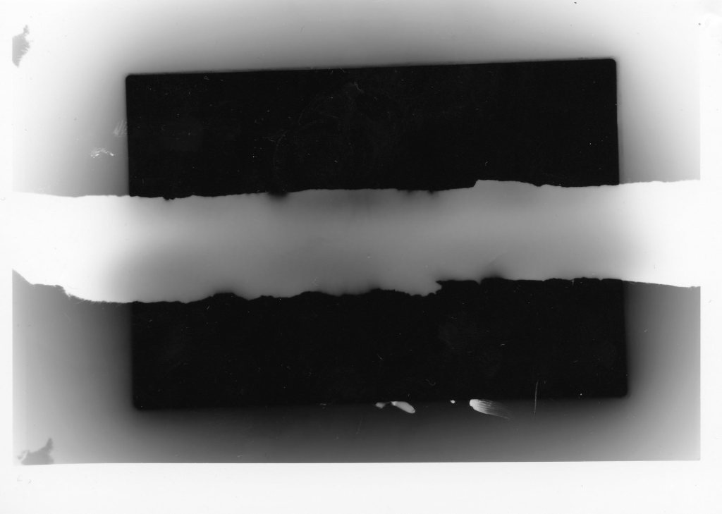 A ruined large format black and white print.   There is a schism where a white scar slashes through a black rectangle. 